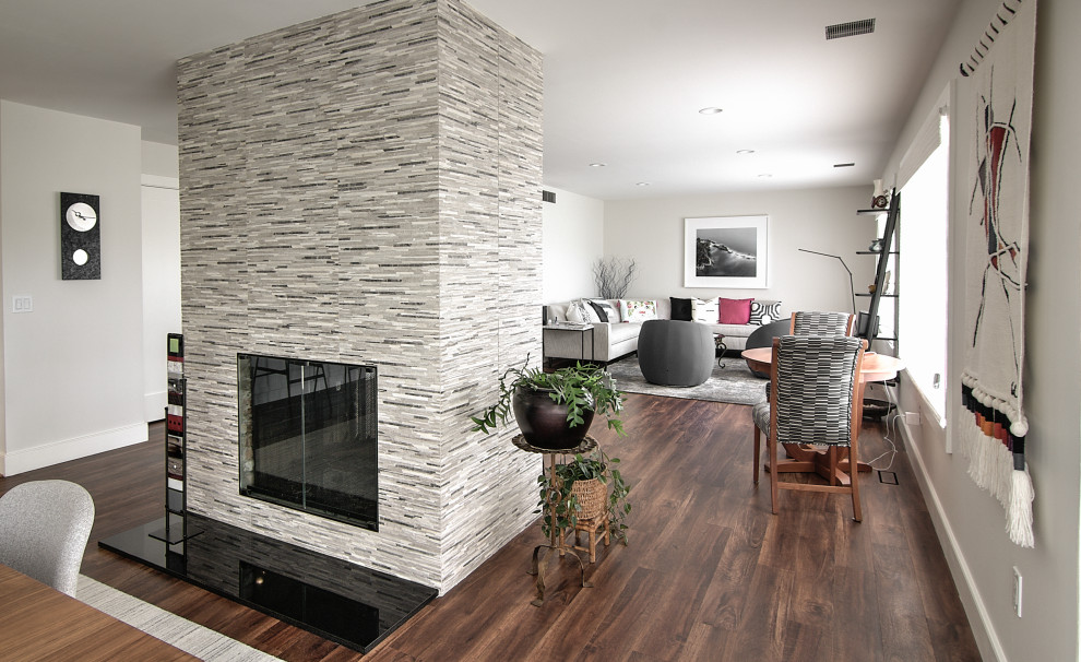 Ejemplo de sala de estar abierta moderna de tamaño medio sin televisor con paredes grises, suelo vinílico, chimenea de doble cara y suelo marrón