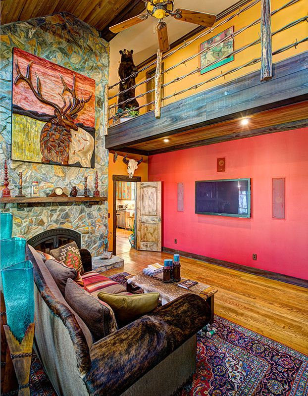 Cette image montre une salle de séjour sud-ouest américain ouverte avec une bibliothèque ou un coin lecture, un mur rouge, parquet clair, une cheminée standard, un manteau de cheminée en pierre, un téléviseur encastré et un sol marron.