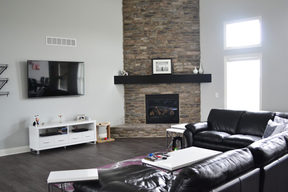 Свежая идея для дизайна: открытая гостиная комната в современном стиле с серыми стенами, полом из керамической плитки, угловым камином, фасадом камина из камня и телевизором на стене - отличное фото интерьера