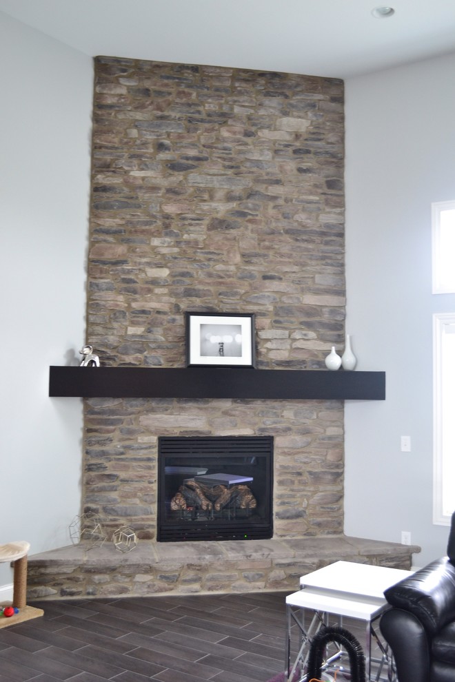 Imagen de salón abierto contemporáneo con paredes grises, suelo de baldosas de cerámica, chimenea de esquina, marco de chimenea de piedra y televisor colgado en la pared