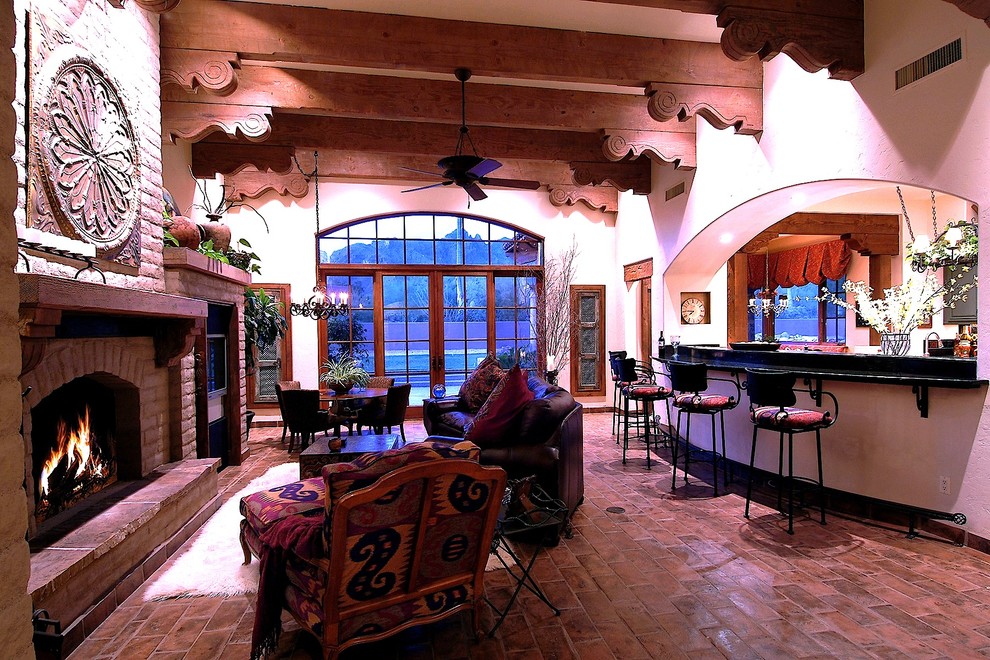 На фото: открытая гостиная комната среднего размера в средиземноморском стиле с домашним баром, бежевыми стенами, полом из терракотовой плитки, стандартным камином, фасадом камина из кирпича и мультимедийным центром с