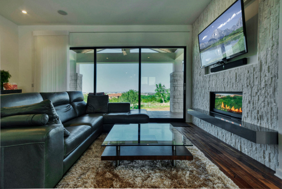 This is an example of a contemporary enclosed games room in Austin with white walls, medium hardwood flooring, a standard fireplace, a stone fireplace surround and a wall mounted tv.