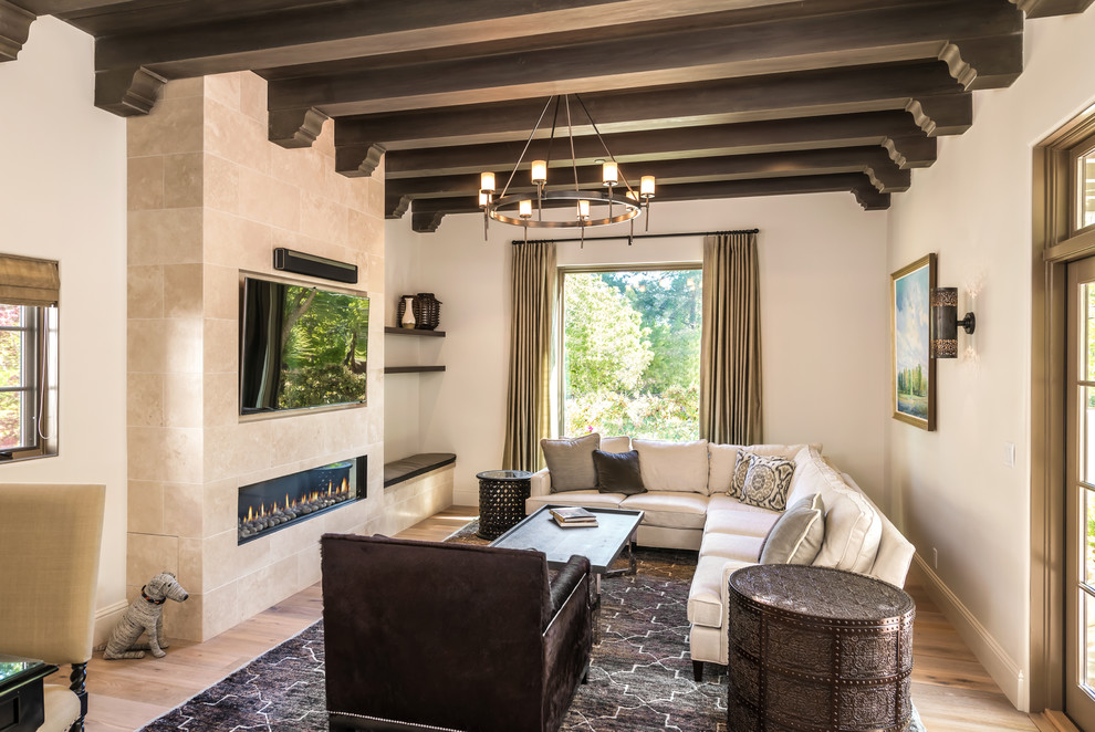 Foto de sala de estar abierta mediterránea con paredes beige, suelo de madera clara, chimenea lineal, marco de chimenea de piedra, televisor colgado en la pared, suelo beige y alfombra