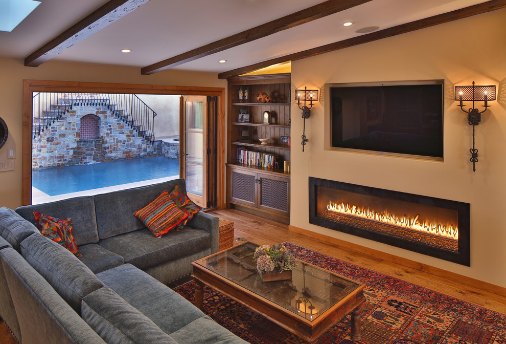 Example of a tuscan medium tone wood floor family room design in Los Angeles with a ribbon fireplace and a wall-mounted tv