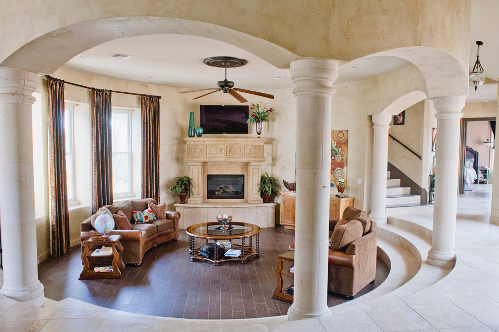 Exemple d'une grande salle de séjour méditerranéenne ouverte avec un mur beige, un sol en carrelage de céramique, une cheminée standard, un manteau de cheminée en pierre et un téléviseur fixé au mur.