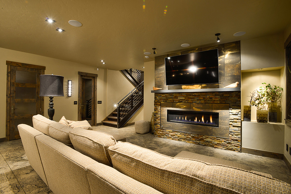Inspiration for a large rustic enclosed concrete floor and gray floor family room remodel in Denver with beige walls, a ribbon fireplace, a stone fireplace and a wall-mounted tv