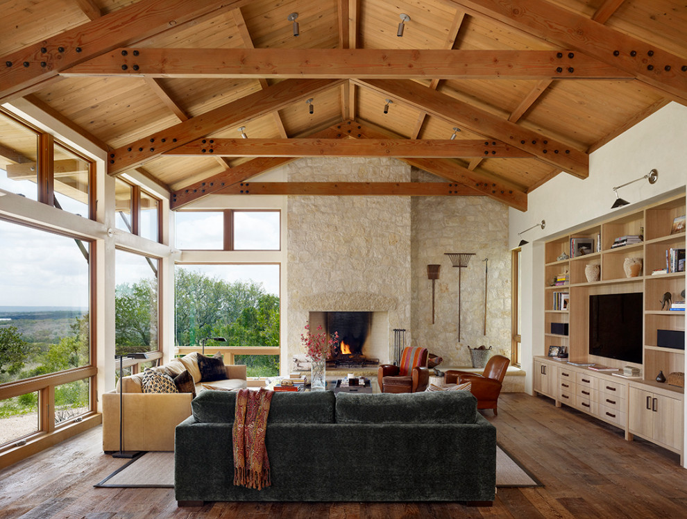 Cette photo montre une grande salle de séjour nature ouverte avec une cheminée standard, un manteau de cheminée en pierre, un téléviseur encastré, un sol marron, un mur blanc, parquet foncé, poutres apparentes, un plafond voûté et un plafond en bois.