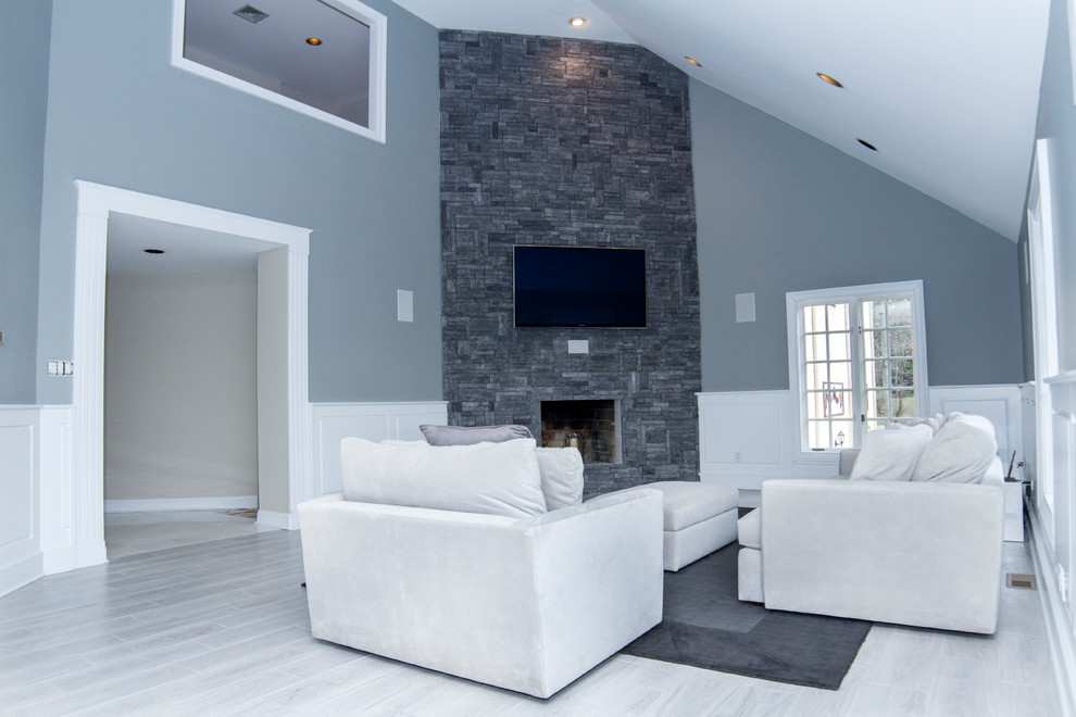 Cette photo montre une salle de séjour tendance de taille moyenne et ouverte avec un mur gris, un sol en carrelage de porcelaine, une cheminée d'angle, un manteau de cheminée en pierre, un téléviseur fixé au mur et un sol gris.