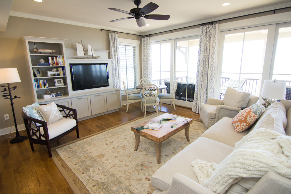 Modelo de sala de estar abierta costera grande sin chimenea con paredes grises, suelo de madera en tonos medios y pared multimedia