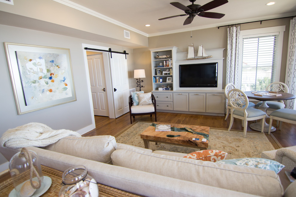 Ejemplo de sala de estar abierta costera grande sin chimenea con paredes grises, suelo de madera en tonos medios y pared multimedia