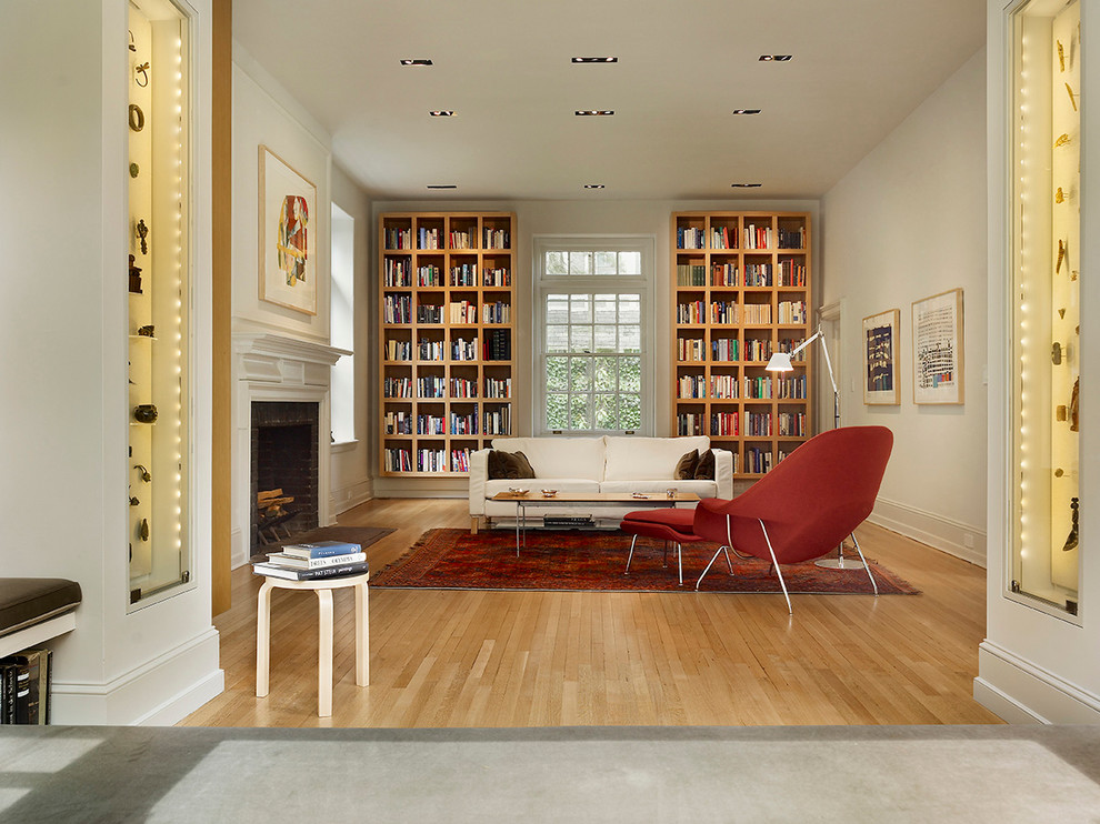 Стильный дизайн: гостиная комната в современном стиле с с книжными шкафами и полками, бежевыми стенами, паркетным полом среднего тона, стандартным камином и ковром на полу без телевизора - последний тренд