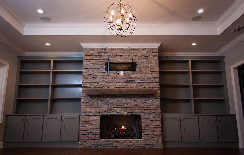 Imagen de sala de estar abierta tradicional grande con paredes grises, suelo de madera oscura, todas las chimeneas, marco de chimenea de piedra y televisor colgado en la pared