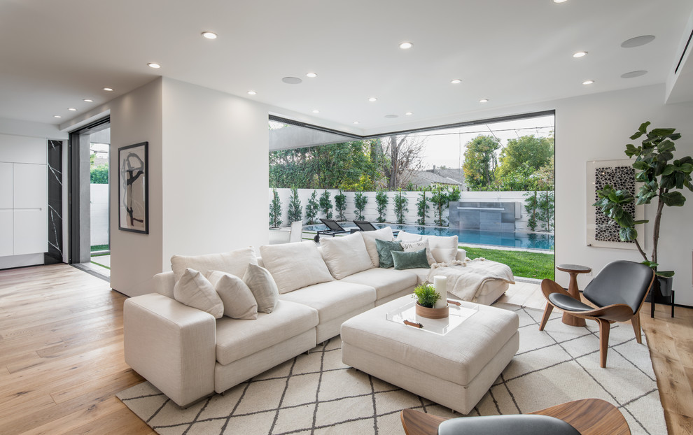 This is an example of a large contemporary open plan living room in Los Angeles with white walls, light hardwood flooring, no tv and beige floors.