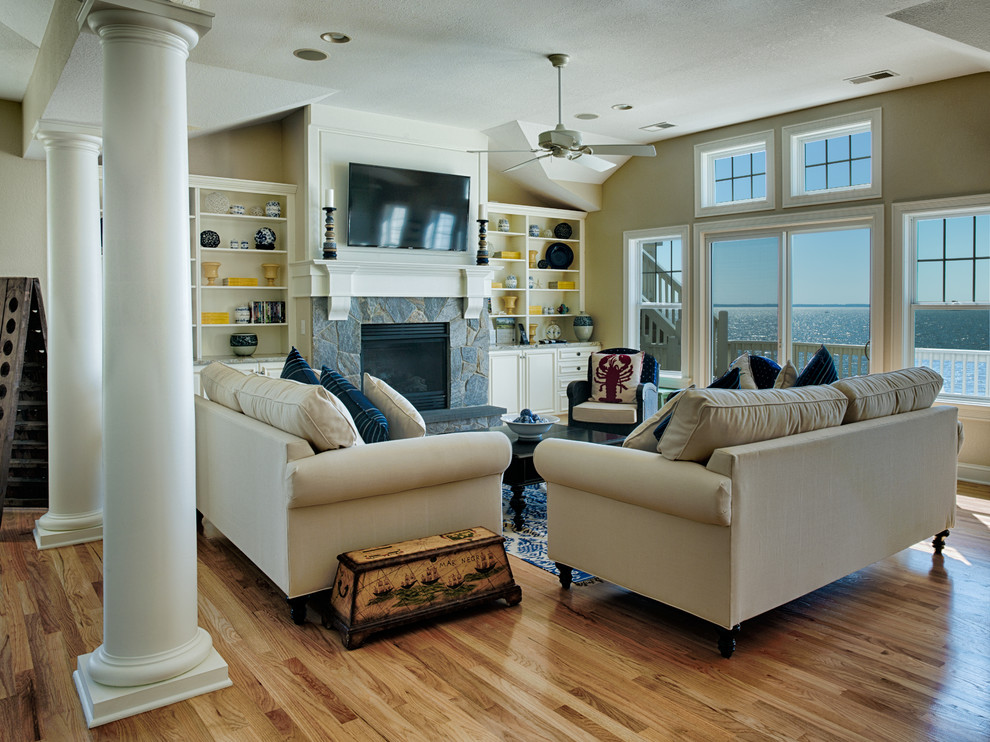 Großes, Offenes Maritimes Wohnzimmer mit beiger Wandfarbe, braunem Holzboden, Kamin, Kaminumrandung aus Stein und TV-Wand in Sonstige
