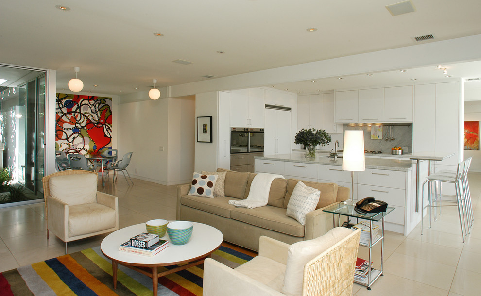 На фото: большая открытая гостиная комната в стиле ретро с белыми стенами, полом из известняка, телевизором на стене и бежевым полом без камина