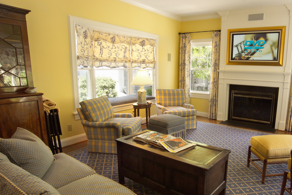Imagen de sala de estar tradicional de tamaño medio con paredes amarillas, suelo de madera en tonos medios, todas las chimeneas, marco de chimenea de madera y televisor colgado en la pared