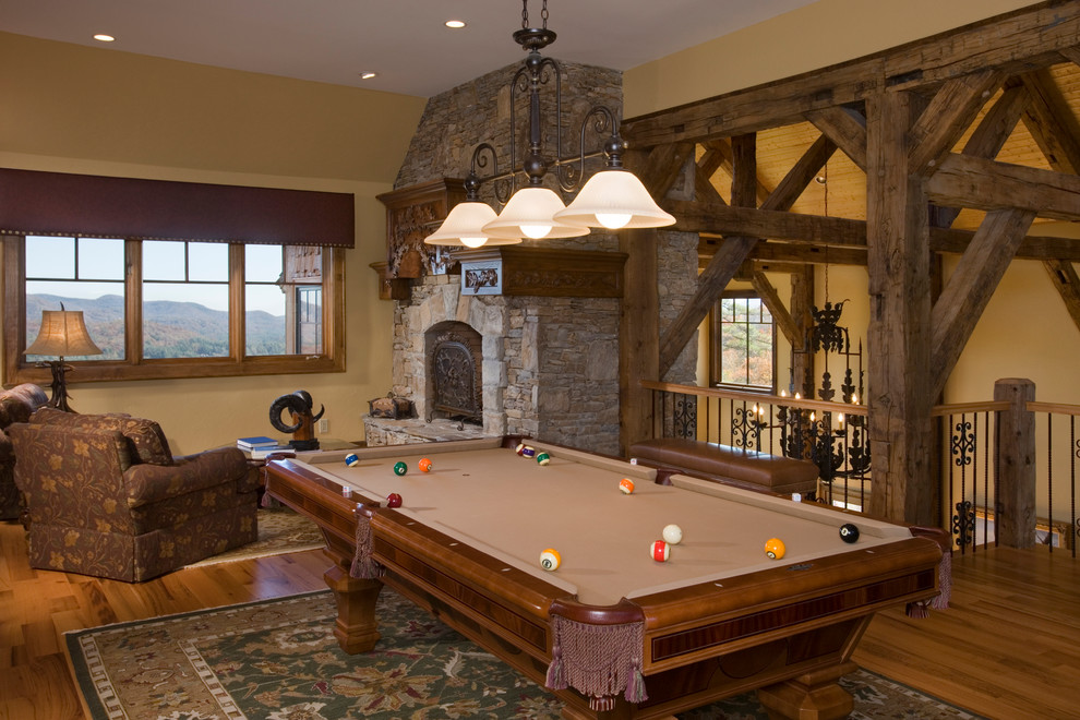 Ejemplo de sala de juegos en casa tipo loft rústica grande con paredes beige, suelo de madera en tonos medios, todas las chimeneas y marco de chimenea de piedra