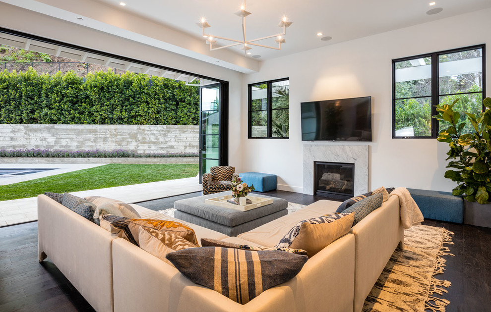ロサンゼルスにある広いコンテンポラリースタイルのおしゃれなオープンリビング (白い壁、無垢フローリング、標準型暖炉、石材の暖炉まわり、壁掛け型テレビ、グレーの床) の写真