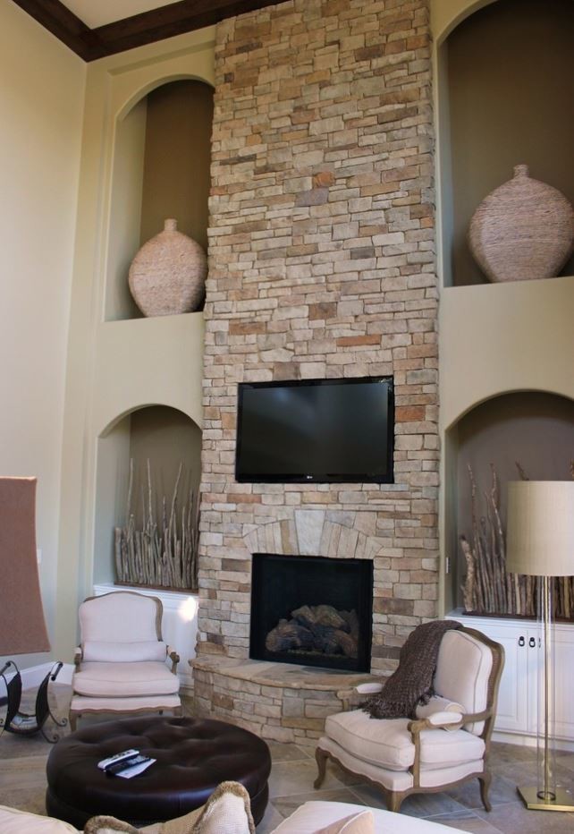 На фото: изолированная гостиная комната в стиле фьюжн с бежевыми стенами, полом из сланца, стандартным камином, фасадом камина из камня, телевизором на стене и бежевым полом с