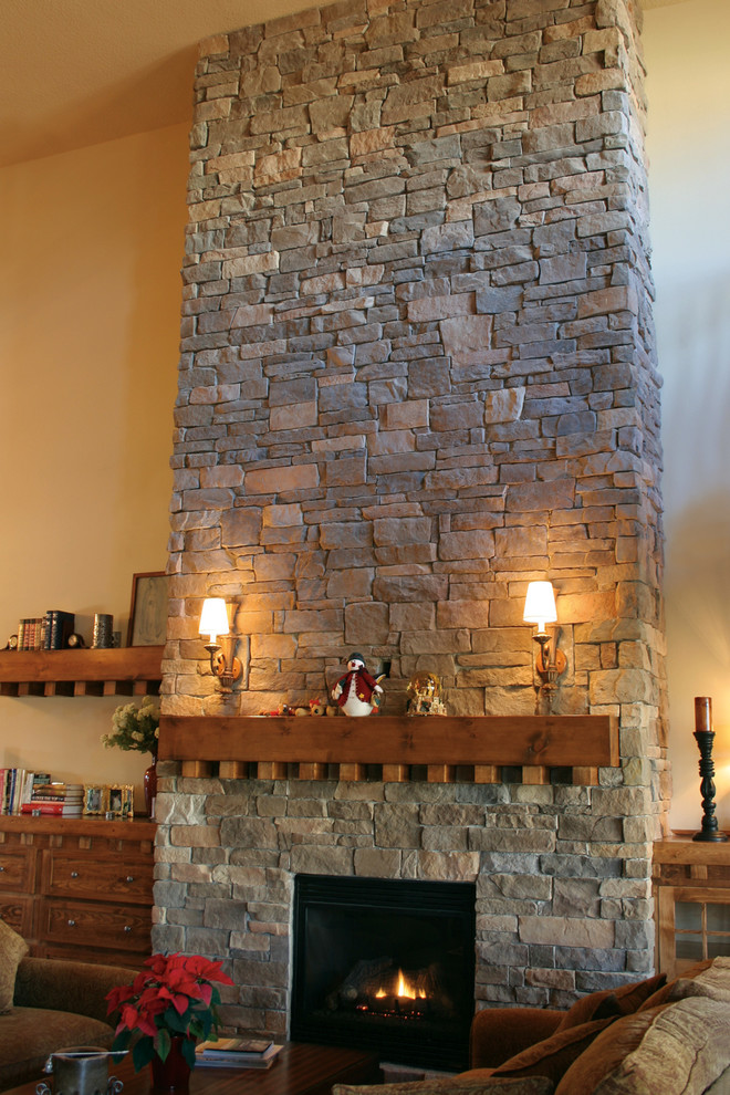 Imagen de sala de estar con biblioteca rural sin televisor con todas las chimeneas, marco de chimenea de piedra, paredes beige y suelo de madera en tonos medios