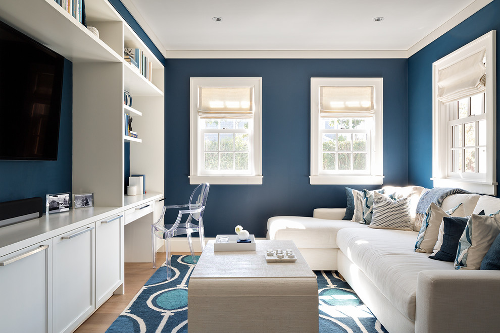Imagen de sala de estar tradicional renovada con paredes azules, suelo de madera clara, televisor colgado en la pared y alfombra