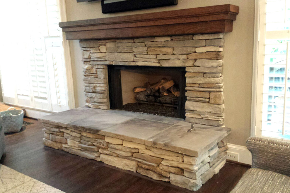 This is an example of a rustic games room in Atlanta with a standard fireplace, a stone fireplace surround, beige walls, dark hardwood flooring, a wall mounted tv and brown floors.