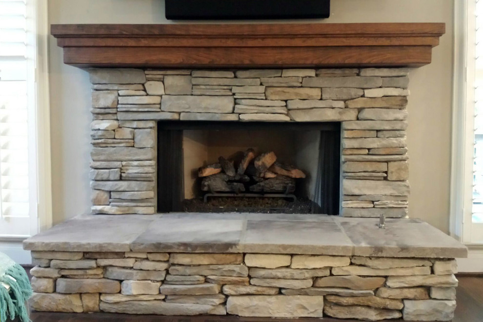 アトランタにあるラスティックスタイルのおしゃれなファミリールーム (標準型暖炉、石材の暖炉まわり、ベージュの壁、濃色無垢フローリング、壁掛け型テレビ、茶色い床) の写真