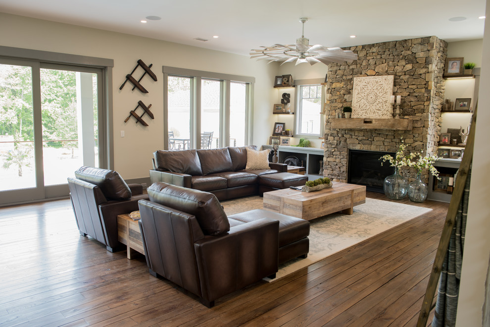 Inspiration for a large rustic open plan games room in Charleston with beige walls, dark hardwood flooring, a standard fireplace, a stone fireplace surround, a wall mounted tv and brown floors.