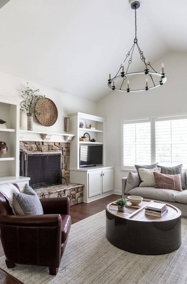 Inspiration pour une salle de séjour traditionnelle avec un mur blanc, parquet foncé, une cheminée standard, un manteau de cheminée en pierre, un téléviseur indépendant, un sol marron et un plafond voûté.