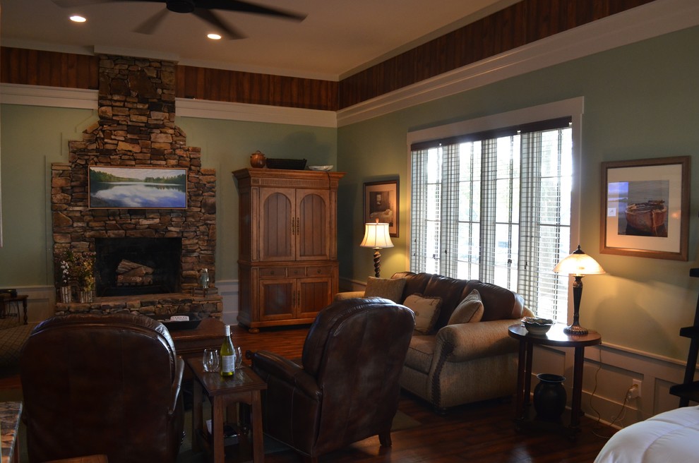 Aménagement d'une salle de séjour montagne de taille moyenne et ouverte avec un mur vert, un sol en bois brun, une cheminée standard, un manteau de cheminée en pierre et un téléviseur fixé au mur.