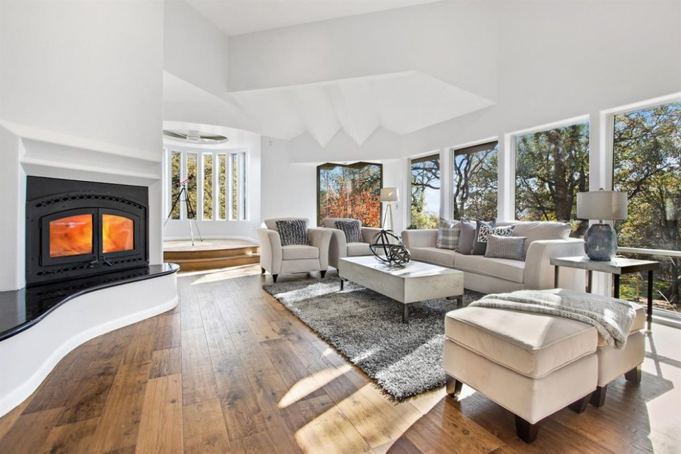 Großes, Fernseherloses, Offenes Modernes Wohnzimmer mit weißer Wandfarbe, braunem Holzboden, Kamin, verputzter Kaminumrandung und braunem Boden in Sacramento