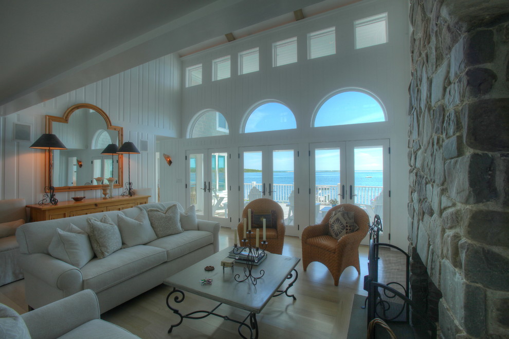 Diseño de sala de estar abierta marinera grande sin televisor con paredes blancas, suelo de madera clara, todas las chimeneas y marco de chimenea de piedra