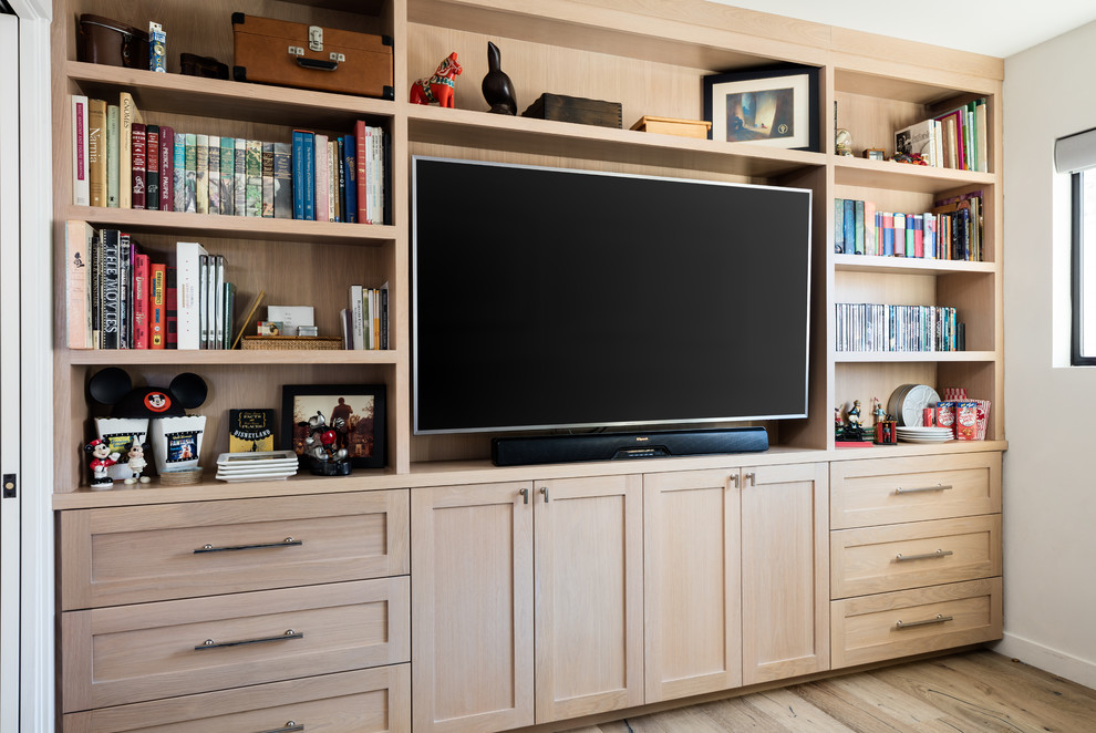 Imagen de sala de estar con biblioteca cerrada clásica renovada pequeña con paredes blancas, suelo de madera clara y televisor colgado en la pared