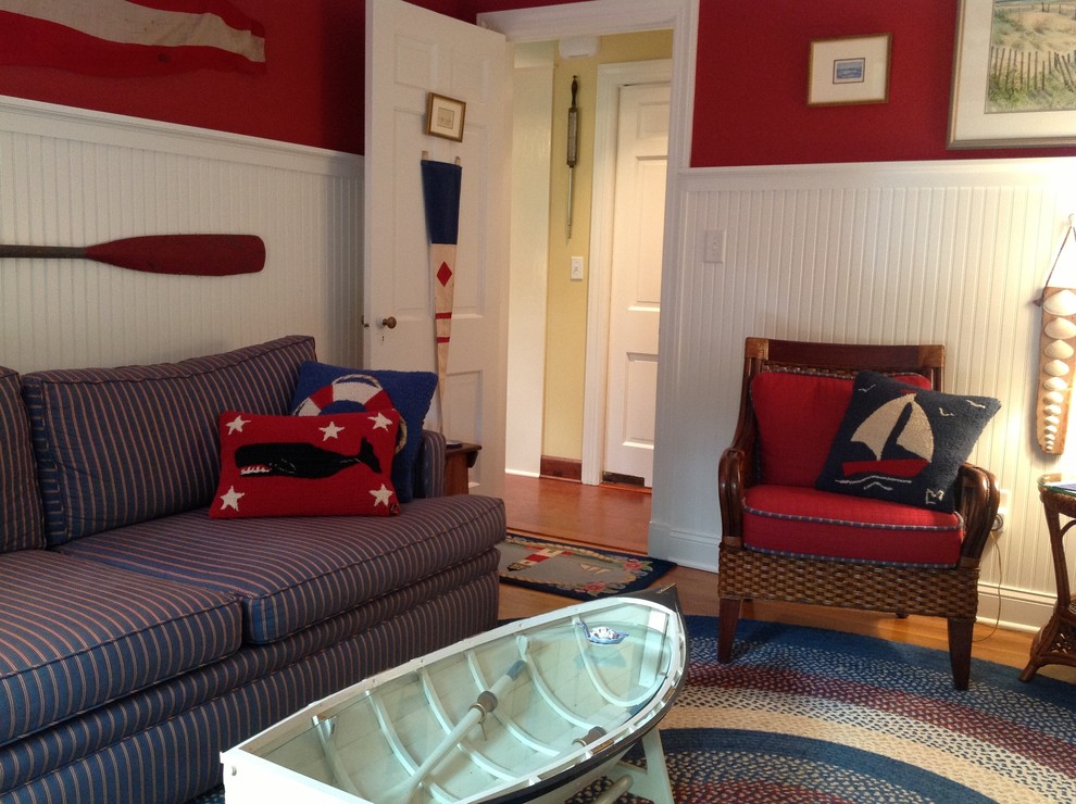 Modelo de sala de estar cerrada costera pequeña sin chimenea y televisor con paredes rojas, suelo de madera en tonos medios y suelo marrón