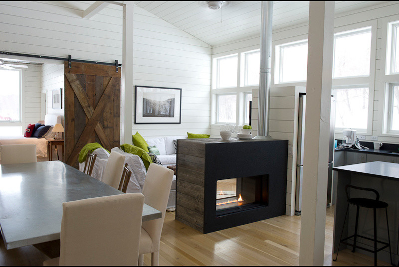 Foto de sala de estar abierta actual de tamaño medio con paredes blancas, suelo de madera clara, chimenea de doble cara y marco de chimenea de madera