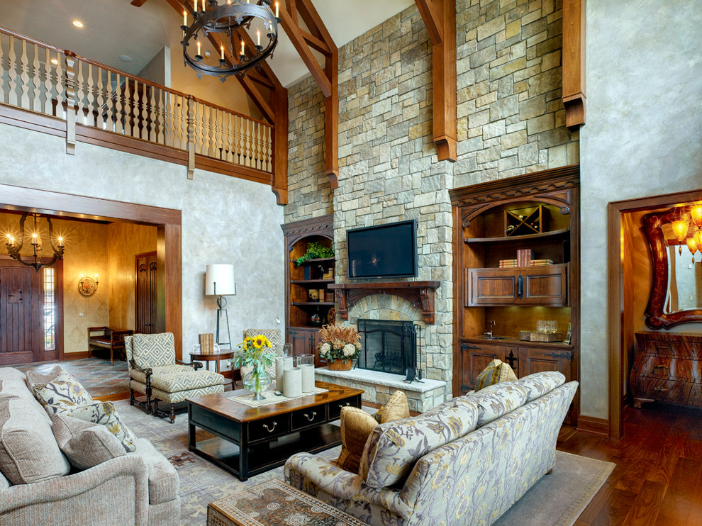 Ejemplo de sala de estar abierta tradicional con paredes grises, suelo de madera oscura, todas las chimeneas, marco de chimenea de piedra y televisor colgado en la pared