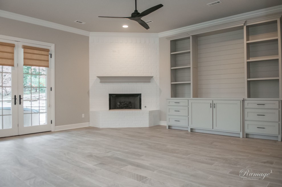 This is an example of a large classic open plan games room in Other with grey walls, porcelain flooring, a corner fireplace, a brick fireplace surround, a built-in media unit and grey floors.