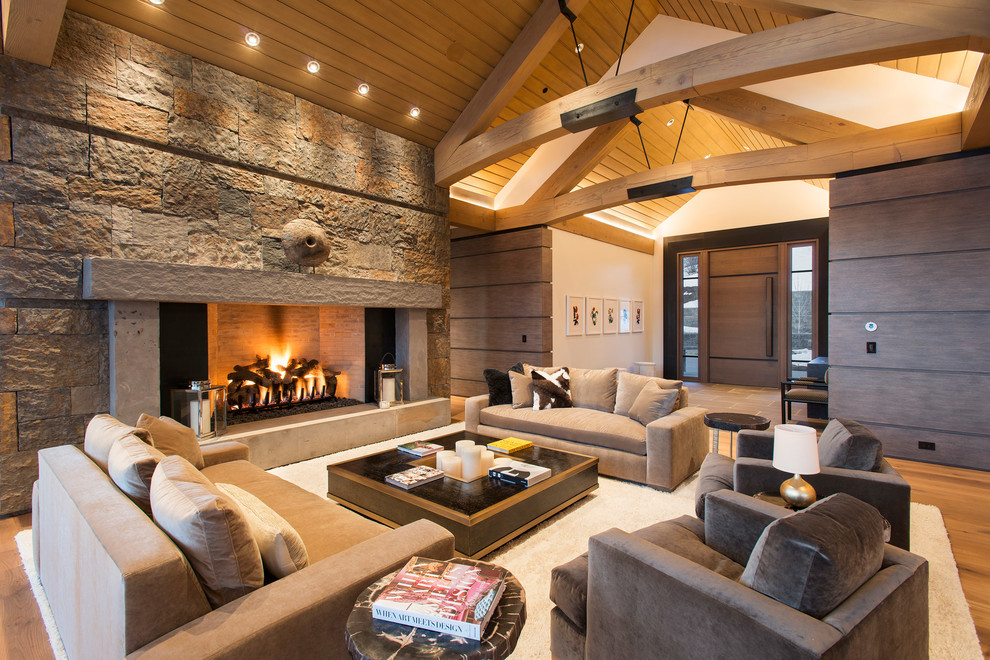 Inspiration pour une très grande salle de séjour design ouverte avec un mur beige, parquet clair, une cheminée standard, un manteau de cheminée en pierre, un téléviseur dissimulé et un sol marron.