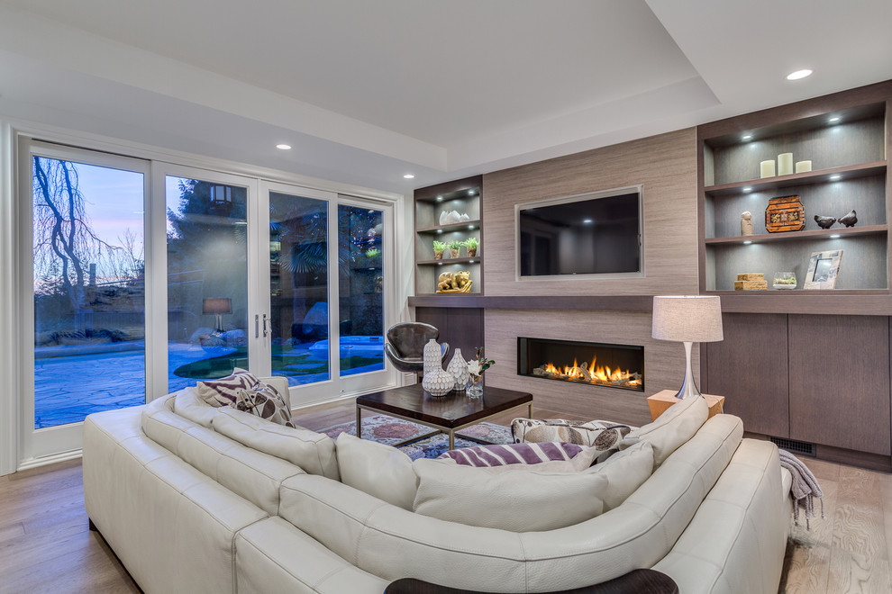 Inspiration for a large timeless open concept light wood floor family room remodel in Vancouver with gray walls, a standard fireplace, a tile fireplace and a wall-mounted tv