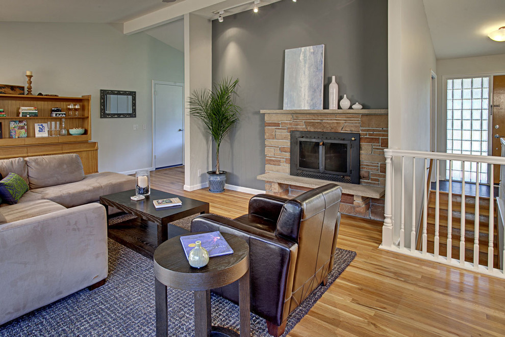 Offenes Klassisches Wohnzimmer mit grauer Wandfarbe, braunem Holzboden, Kamin und Kaminumrandung aus Stein in Seattle
