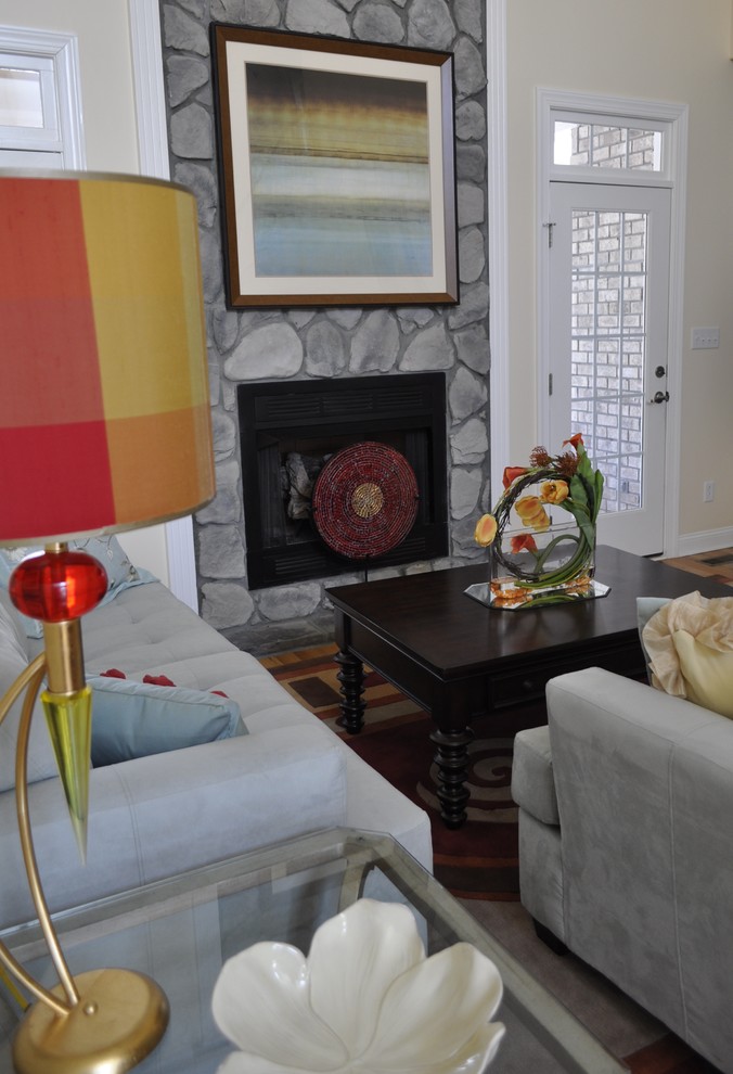 Exemple d'une salle de séjour tendance ouverte et de taille moyenne avec un mur jaune, un sol en bois brun, une cheminée standard, un manteau de cheminée en pierre et un téléviseur dissimulé.