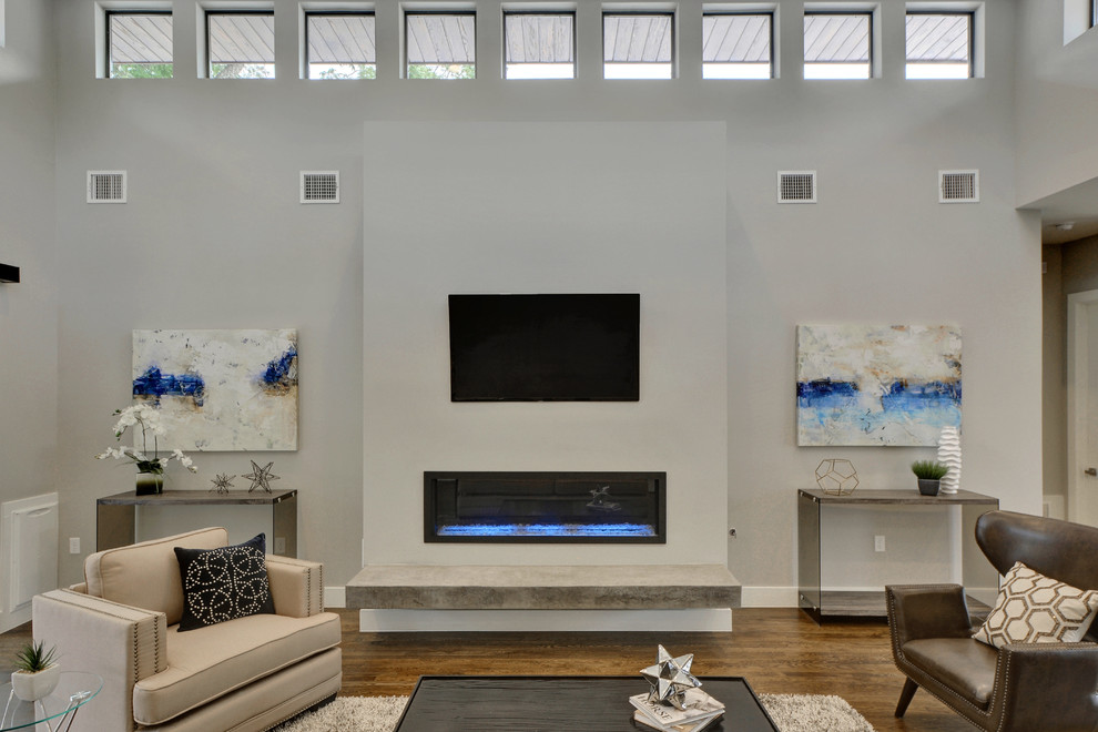 Großes, Offenes Modernes Wohnzimmer mit grauer Wandfarbe, braunem Holzboden, Gaskamin, Kaminumrandung aus Beton und TV-Wand in Austin