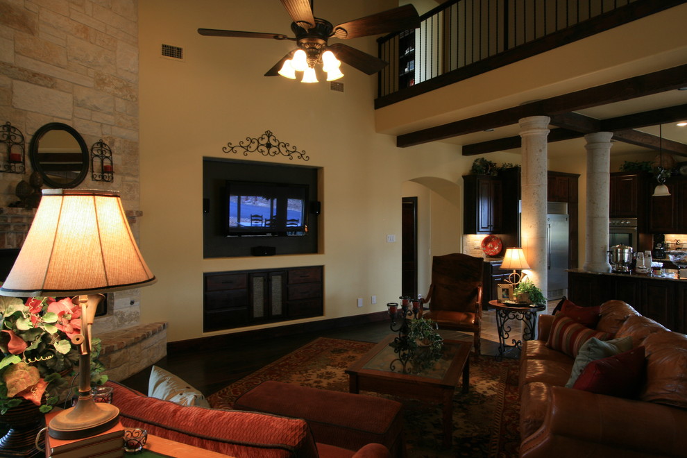 Пример оригинального дизайна: большая открытая гостиная комната в средиземноморском стиле с бежевыми стенами, темным паркетным полом, угловым камином, фасадом камина из камня, телевизором на стене и коричневым полом
