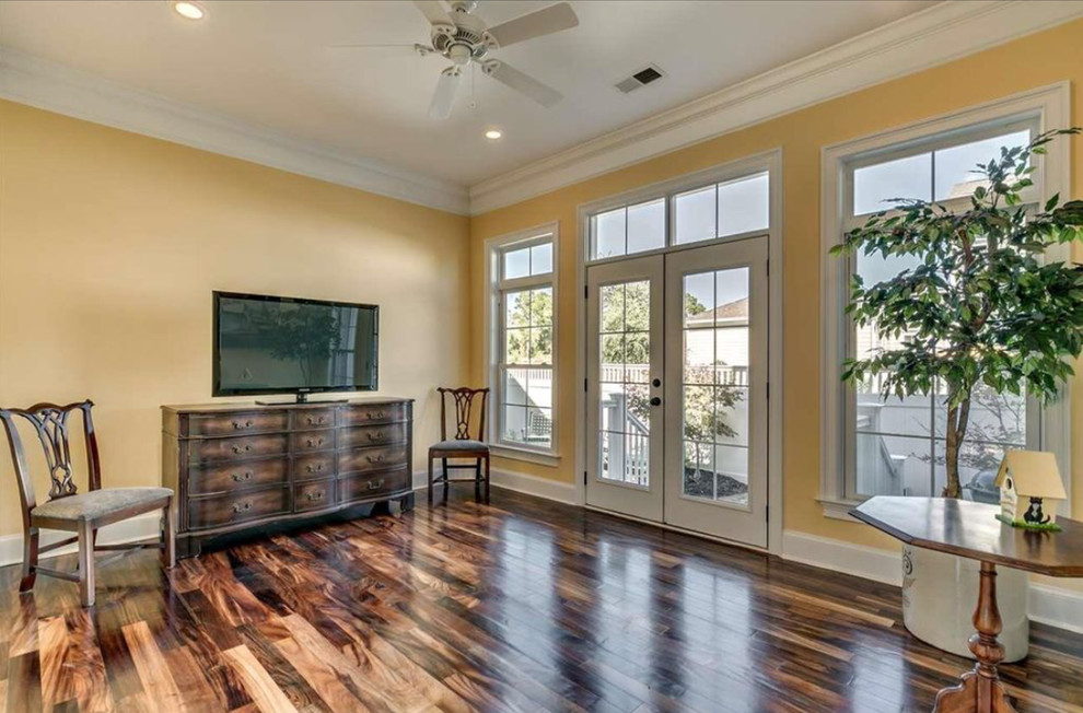 Foto de sala de estar abierta tradicional renovada de tamaño medio sin chimenea con paredes amarillas, suelo de madera en tonos medios, televisor independiente y suelo marrón