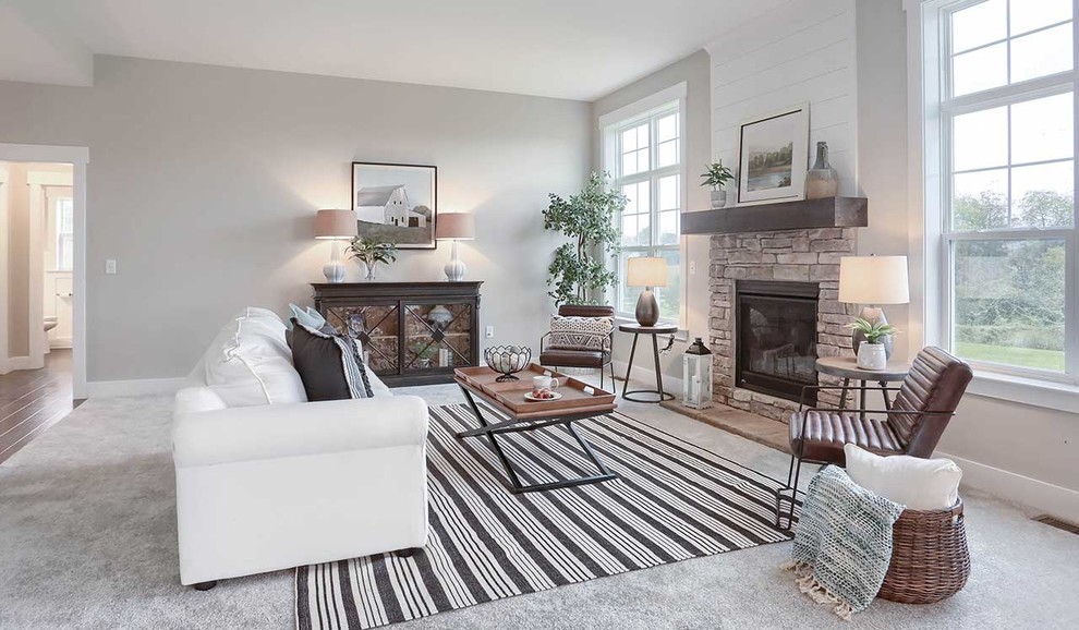 Modelo de sala de estar abierta de estilo de casa de campo grande con paredes grises, moqueta, todas las chimeneas, marco de chimenea de piedra y suelo beige