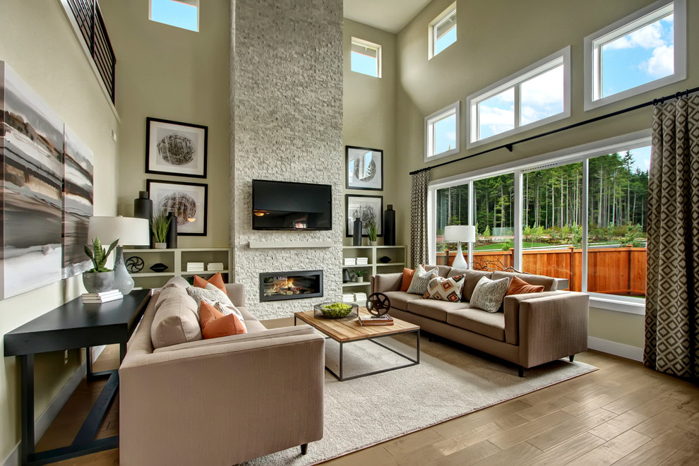 Diseño de sala de estar abierta de estilo americano con paredes grises, suelo de madera clara, todas las chimeneas, marco de chimenea de piedra y televisor colgado en la pared