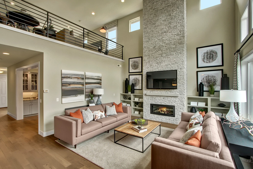 Imagen de sala de estar abierta de estilo americano con paredes grises, suelo de madera clara, todas las chimeneas, marco de chimenea de piedra y televisor colgado en la pared