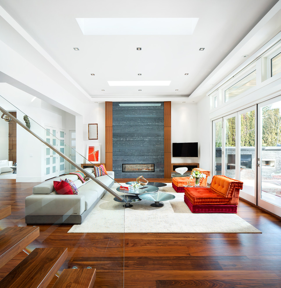 Mittelgroßes, Offenes Modernes Wohnzimmer mit weißer Wandfarbe, Tunnelkamin, Kaminumrandung aus Stein, braunem Holzboden, TV-Wand und braunem Boden in Vancouver