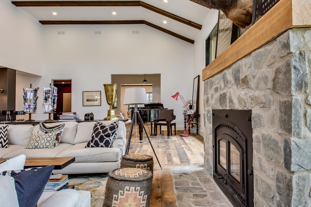 This is an example of an expansive farmhouse open plan games room in Calgary with a music area, white walls, medium hardwood flooring, a wood burning stove, a stone fireplace surround, no tv and multi-coloured floors.