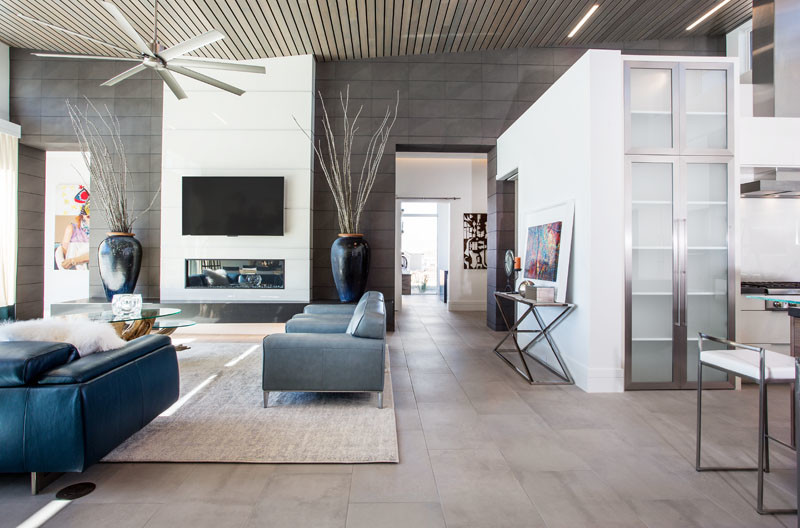 Modelo de sala de estar abierta moderna grande con paredes blancas, suelo de baldosas de cerámica, chimenea lineal, marco de chimenea de metal y televisor colgado en la pared
